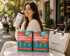 A woman sitting at an outdoor cafe table holds a white Optivance travel cup while two boxes of Optivance Mummy Smoothie and a white Optivance tote bag are displayed in the foreground.