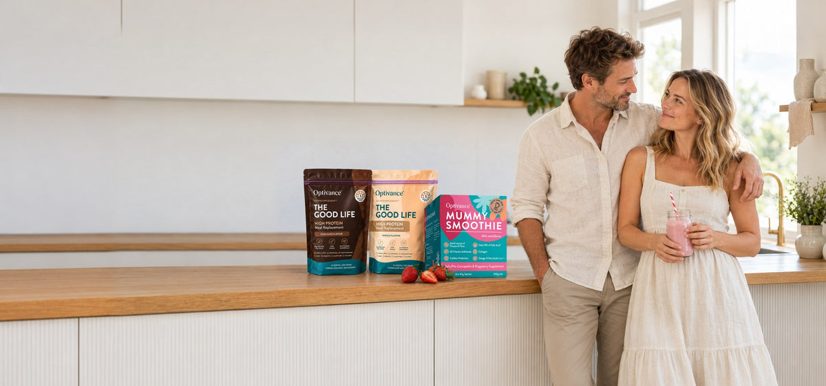 A couple in their thirties at a sunlit kitchen bench beside two pouches of THE GOOD LIFE NutraSupplement and a Mummy Smoothie box